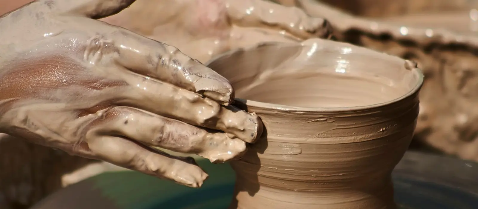A pair of clay-covered hands opening the rim of a bowl on a spinning wheel.